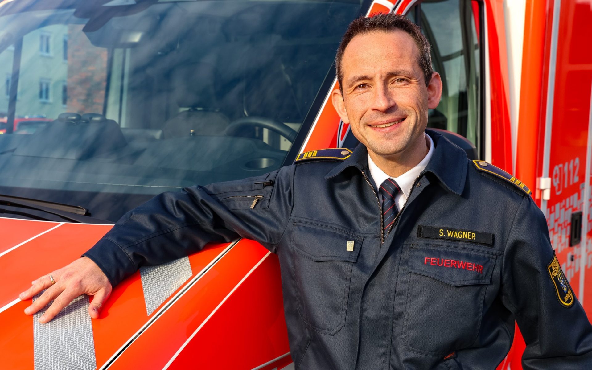 Hochwertiges Bild eines Feuerwehrchefs in Uniform vor einem Einsatzfahrzeug, Symbol für Einsatzbereitschaft und Rettungsdienst in Solingen.