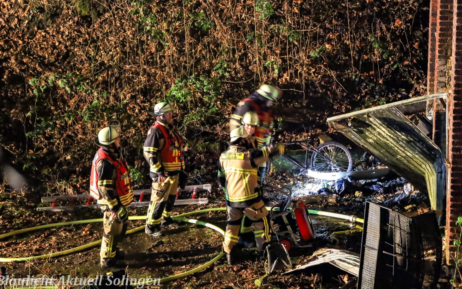 Einsatzwagen der Feuerwehr und Feuerwehrleute bei nächtlichem Rettungseinsatz in Solingen.